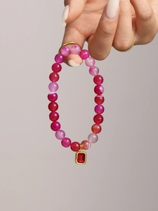 Detail view of pink agate bead bracelet with a gold-edged square red gemstone pendant
