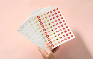 Close-up of hand holding multiple sheets of cute cartoon reward stickers for students