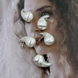 Set di quattro orecchini a goccia in argento opaco spazzolato su sfondo poster di modella