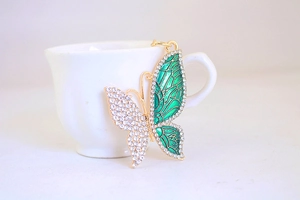 Close-up of golden butterfly keychain with green enamel wing and sparkling rhinestones