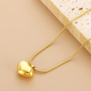 Collier avec pendentif cœur doré et chaîne serpent sur pierre avec fond beige épuré
