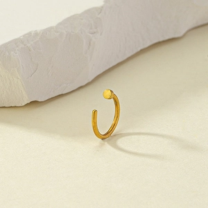 Macro shot of gold-plated C-shaped nose ring with flat disk on a textured beige surface
