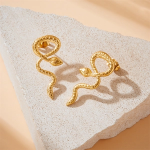 Golden stainless steel snake earrings with scale texture on textured stone background