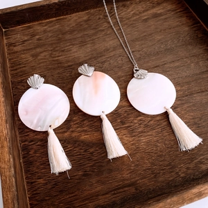 Detailed shot of jewelry set with round resin pendants and cream tassels on wood tray