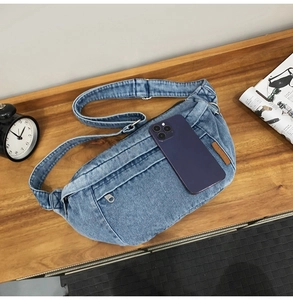 Top view of blue denim crossbody bag on wood table with a phone for size reference