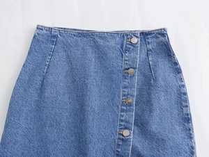 Dettaglio ravvicinato di gonna midi in denim blu con fila di bottoni centrale frontale