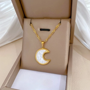 Detail of a gold crescent moon pendant with white shell inlay in a beige jewelry box