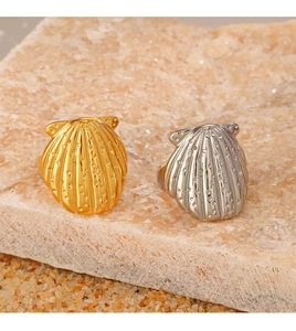 Detailed view of gold and silver shell-shaped rings on beach sand and stones