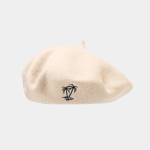 Detailed close-up of beige wool beret featuring black coconut tree embroidery detail