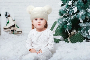 Detail of white knit hat with double oversized pom-poms for kids in Christmas setting