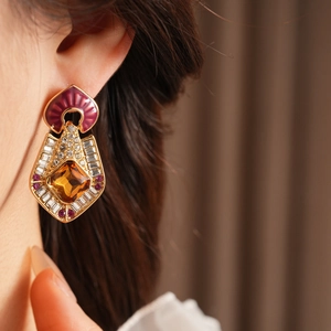 Close-up of golden rhombus earrings with purple enamel and amber gemstone inlay