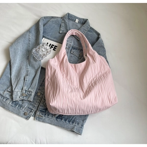 Nahaufnahme der rosa Plissee-Tasche auf weißem Laken mit Jeansjacke und Lifestyle-Dekoration