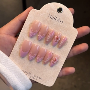 Macro view of almond press-on nails with 3D embossed flowers and gold beads on card