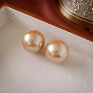 Macro shot of champagne round faux pearl earrings on white velvet jewelry tray