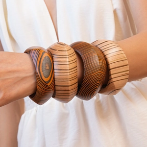 Detailed view of four wide wooden bangles with natural grain textures on a model's wrist