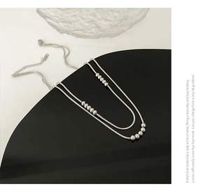 Close-up of a minimalist silver double-layer snake chain necklace with bead details