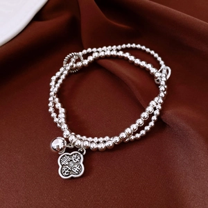 Double-layer silver beaded bracelet with bell and flower pendant on dark brown fabric