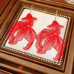 Détail de boucles d'oreilles carpes rouges sur tissu beige dans un cadre en bois