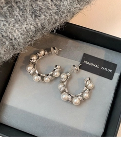 Detail of silver C-shape pearl earrings with micro-set zircons on dark velvet