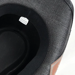 Detail of woven black paper straw cowboy hat with brown leather band and blue stitching