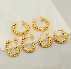 Close-up of golden twisted rope hoop earrings on white marble, minimalist vintage jewelry