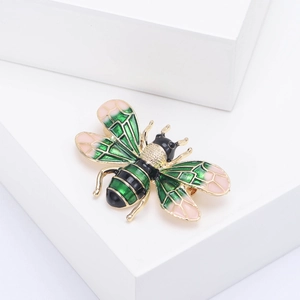 Detail shot of golden honey bee brooch with green, black, and pink enamel on a white stand