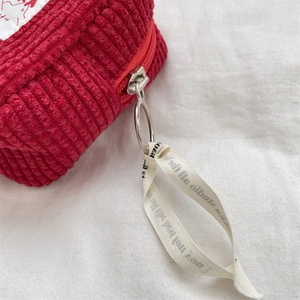 Close-up of red corduroy pouch with silver metal zipper and printed ribbon strap