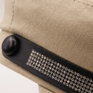 Close-up of sparkling rhinestones on black leather trim of a beige baker boy hat