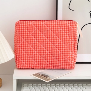 Detailed view of red gingham quilted cosmetic bag with ribbon zipper on a desk