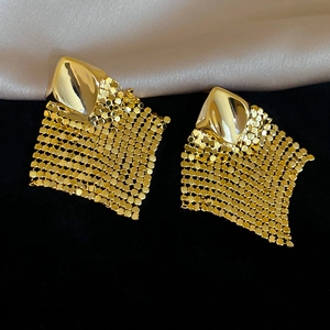 Close-up of golden geometric mesh rhombus tassel earrings on elegant fabric background