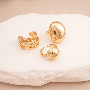 Three-piece gold geometric ring set with smooth pebble shapes on natural stone