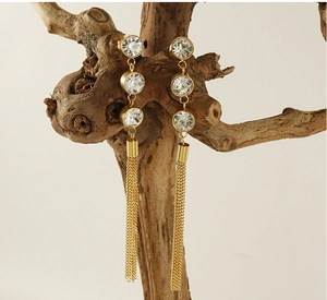Dettaglio di orecchini lunghi a nappa dorati con zirconi su un ramo di legno naturale