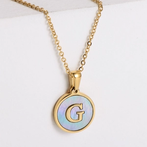 Detail shot of round 18k gold plated necklace with blue shell inlay and letter G