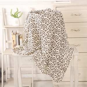 Close-up detail of leopard print muslin cotton baby blanket draped over a vintage wood table