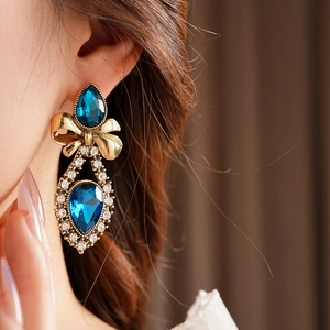 Detailed close-up of a vintage golden bow earring featuring a blue teardrop gemstone