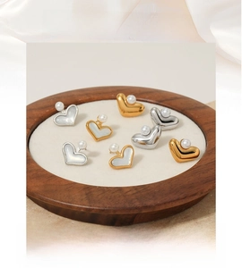 Dettaglio di orecchini a perla a forma di cuore in oro e argento su un vassoio di legno