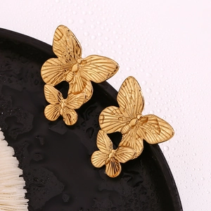 Macro shot of 18K gold plated double butterfly earrings on a dark textured tray