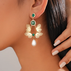 Detailed view of butterfly earrings with green crystals and drop pearl on model