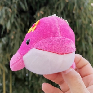 Close-up detail of a cute pink and white whale plush keychain with a small yellow flower
