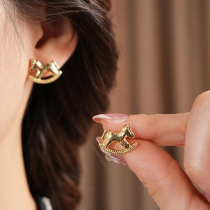 Close-up of gold rocking horse stud earrings with zircon and pearl details on model