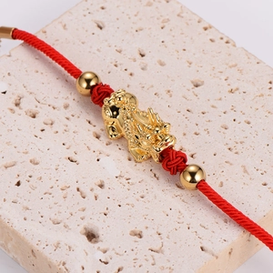 Traditional red string bracelet with gold Pixiu pendant and beads on stone pedestal