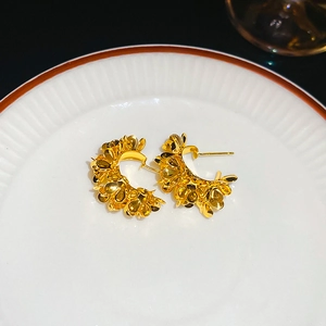 Close-up of golden C-shaped flower earrings with metallic petals on ceramic display