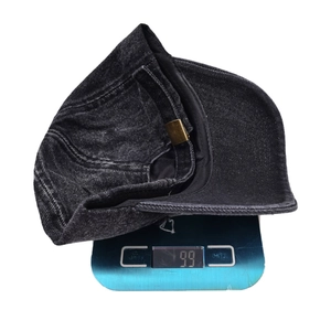 Vintage black distressed denim baseball cap with adjustable metal buckle on a scale