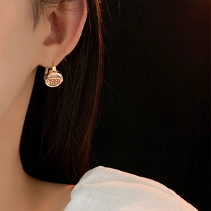 Close-up of gold-finish hoop earring featuring a red enamel M design on the model