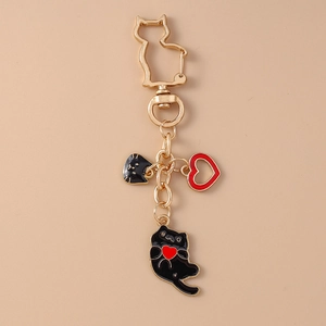 Detail of a gold cat keychain with black enamel feline and red heart charms on pink background