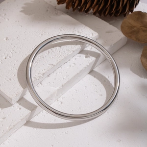 Polished silver stainless steel round bangle placed on a textured white stone surface