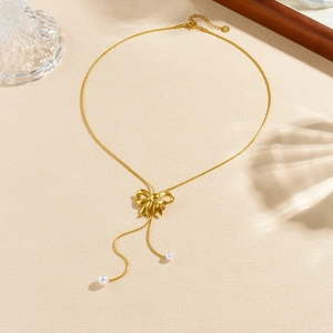 Golden bow pearl Y-necklace displayed in a heart shape on a textured beige surface
