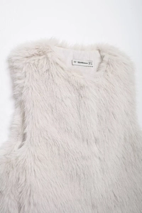 Detail view of the inner neck label showing M size on a fuzzy cream faux fur vest