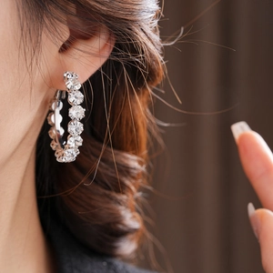 Macro shot of silver diamond-encrusted hoop earrings worn on ear with high-end shimmer