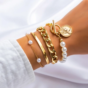 Detail of four-piece gold bracelet set with pearls and coin pendant on a model wrist